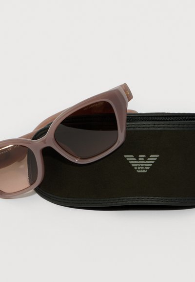 Růžové sluneční brýle odpočívající na černém pouzdře značky Giorgio Armani s jemným logem na přední straně.