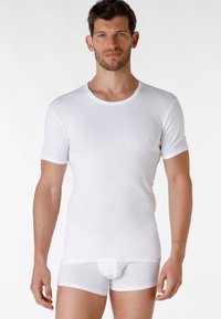 Maglietta bianca a maniche corte con scollo rotondo, realizzata in tessuto morbido. Indossata con slip bianchi semi-trasparenti, che mettono in risalto un design attillato.