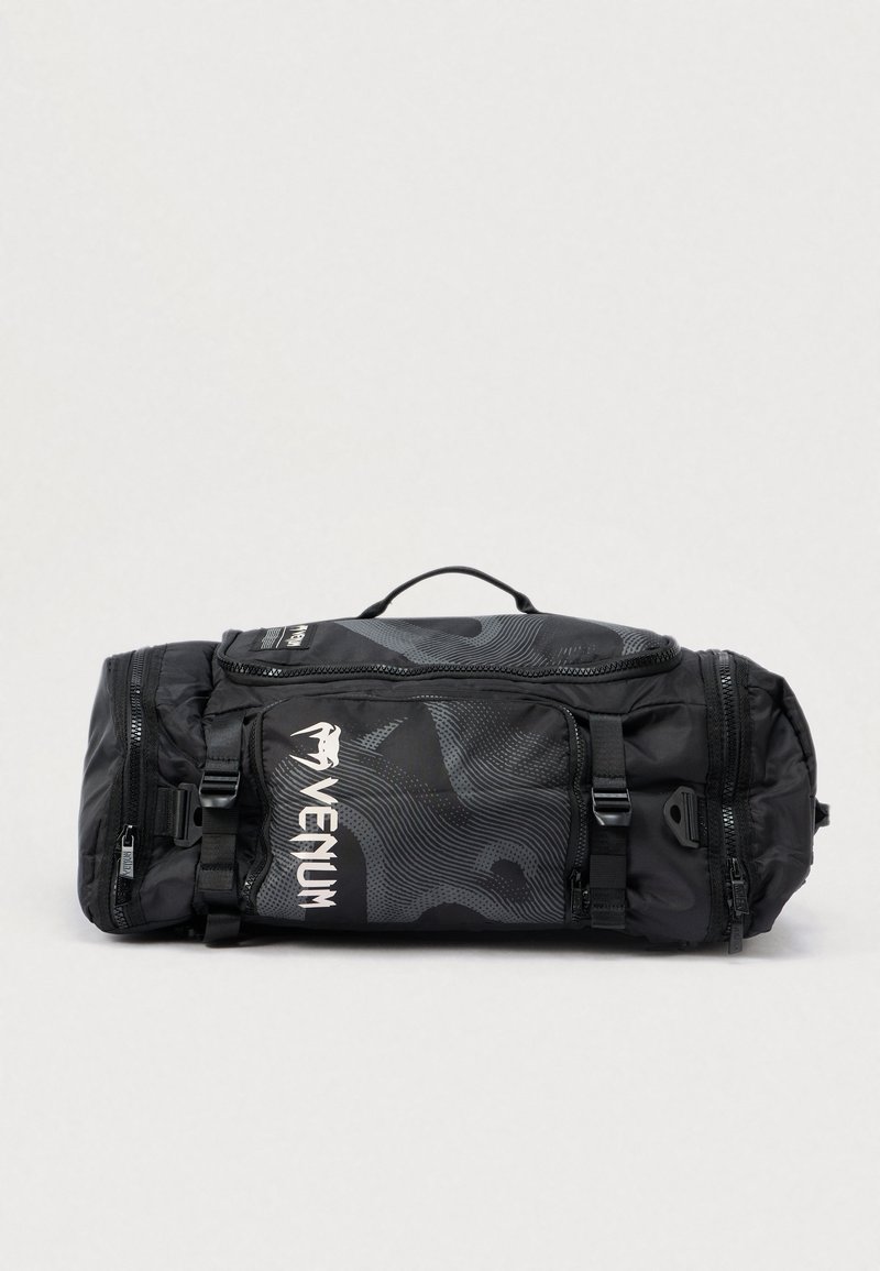 Mustast kangast spordikott sileda tekstuuriga, millel on stiliseeritud geomeetriline muster, logo, kaks tõmblukku ja reguleeritavad rihmad.