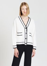 Cardigan bianco con rifiniture nere, scollo a V e tasche frontali. I bottoni anteriori ne migliorano la funzionalità. Texture morbida e vestibilità rilassata.