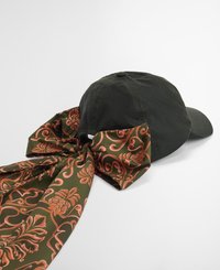Boné de beisebol verde escuro com uma grande fita de tecido estampada em tons de oliva e coral, apresentando desenhos florais e em espiral.