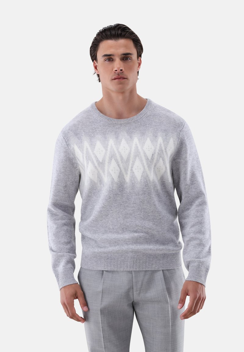 Grau gestrickter Pullover aus Wolle mit einem Rautenmuster in Creme, rundem Ausschnitt und gerippten Bündchen. Getragen mit hellgrauen Hosen.