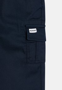 Marinblå cargobyxor med en sidficka med spetsad flik och en "HILFIGER"-etikett. Smidigt tyg med lätt textur.