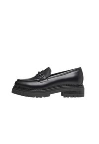 Mocassins en cuir noir avec une semelle en caoutchouc épaisse, dotées d'une sangle décorative et de coutures le long du côté supérieur.