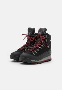 Botas de senderismo negras con acentos rojos, materiales de cuero y textil, ojales metálicos, suelas robustas y cordones gruesos para un ajuste seguro.