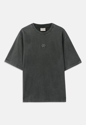 T-shirt gris foncé avec logo, shorts beiges, chaussettes blanches et baskets claires. Mannequin portant des lunettes de soleil noires. Coupe simple et décontractée.