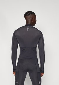 Haut noir à manches longues avec une finition texturée et une coupe ajustée. Présente un logo au dos et un bas ajusté avec des détails accentués.