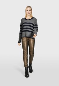 Šedý a námořnický pruhovaný svetr s kulatým výstřihem, spárovaný s lesklými bronzovými těsnými kalhotami a černými robustními botami. Jednoduché pozadí.