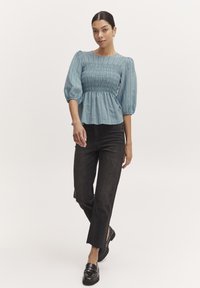 Blå smockblus med puffärmar, lättviktig tyg, texturerad front. I kombination med högmidjade svarta denim och kraftiga svarta skor.