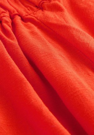 Röd linnetyg med en texturerad yta, med inslag av rynkade detaljer. Tyget visar en rik, livlig färg och mjukhet.