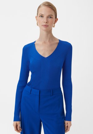 Blaues geripptes Langarmoberteil mit V-Ausschnitt, aus strukturierter Strickmaterial gefertigt, kombiniert mit passenden blauen Hosen.