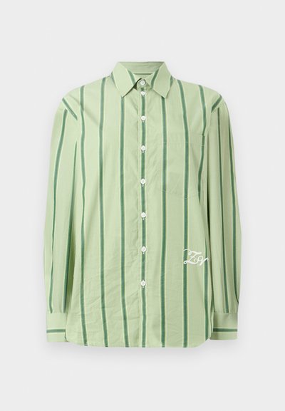 Ανοιχτό πράσινο πουκάμισο με μακριά μανίκια και κάθετες σκούρες πράσινες ρίγες, λευκά κουμπιά, τσέπη στο στήθος και λευκή κεντημένη γραφή κοντά στο τελείωμα.