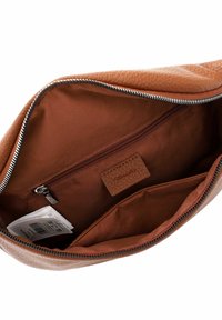 Interiér hnědé kožené tašky má hladkou texturu, zapínání na zip, jednu kapsu na zip a štítek. Podšívka je světle hnědé barvy.