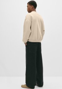 Hanorac oversized de culoare crem, cu umeri căzuți, asortat cu pantaloni din denim negri, cu picioare largi. Încălțămintea în nuanțe neutre completează ținuta.