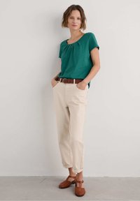 Camicetta corta color teal con dettagli arricciati, pantaloni crema con risvolti e scarpe intrecciate marroni. Design semplice e rilassato.