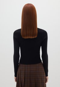 Haut noir à manches longues côtelé avec une silhouette ajustée, associé à une jupe à carreaux marron avec des plis et des lignes de couleur contrastante.