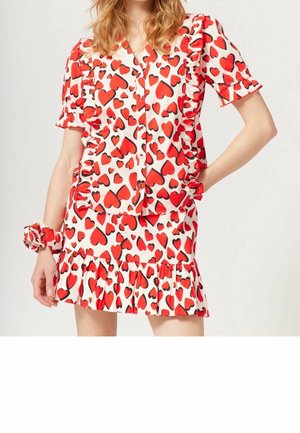 Abito a maniche corte con motivo a cuori rosso e nero su sfondo bianco. Presenta bordi arricciati e un orlo svasato. Incluso accessorio scrunchie.