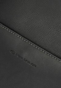 Portefeuille en cuir noir avec une surface texturée. Présente une couture lisse et un logo embossé. Design compact aux lignes épurées.
