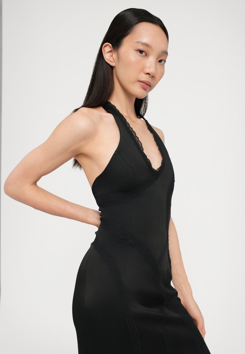 Black halter neck dress made of sleek fabric with lace trim detailing. Form-fitting design with V-neck and intricate seams.