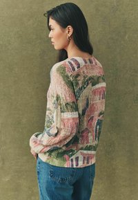 Kleurrijke gebreide trui met bloemmotieven in roze, groen en blauw, met een ontspannen pasvorm en textiele stof, gedragen met denim jeans.