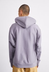 Grey hooded sweatshirt with a relaxed fit, textured fabric, dropped shoulders, and ribbed cuffs. Seam detailing along the back.