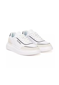 Baskets blanches montantes avec semelles épaisses, bordures noires, accents en daim, lacets et un logo métallique sur le côté.