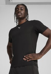Cămășuță sport neagră cu mânecă scurtă, confecționată dintr-un material ușor, cu un design ajustat. Prezintă un logo alb Puma pe piept și o textură netedă.