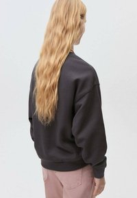 Mörkgrå sweatshirt med rund halsringning, sänkta axlar och ribbade ärmslut, tillsammans med ljusrosa byxor. Mjuk struktur och avslappnad passform.