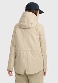 Beige wasserdichte Jacke mit hohem Kragen und verstellbarem Kapuze. Merkmale sind lange Ärmel und ein belüfteter Rückensaum. Minimalistischer Stil ohne sichtbare Hardware.