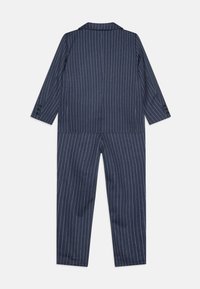 Tume sinine triibuline jumpsuit, millel on nurgelise kraega, pikad varrukad ja nööbid mansettide peal; sile tekstuur ja kohandatud lõige.
