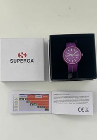 Fialová silikónová hodinky s okrúhlym čelom, bielymi hodinovými značkami a textom "SUPERGA". Obsahuje bielu krabicu a návod na použitie.