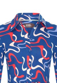 Sininen puuvillapaita, jossa on nappikaulus, ja jossa on värikäs abstrakti kuvio punaisena, vaaleanpunaisena ja vaaleansinisenä.