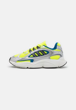 Sneaker atletiche giallo neon e grigie con materiali in rete e sintetici, caratterizzate da una spessa soletta bianca e dettagli neri sulla suola.