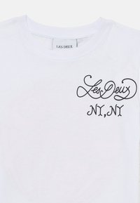 Weißes Baumwoll-T-Shirt mit schwarzem geschwungenem Text "Les Deux" und "NY, NY" im linken Brustbereich. Klassischer Rundhalsausschnitt und kurze Ärmel.