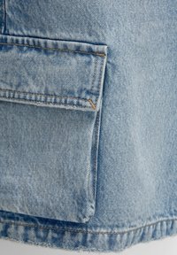 Tissu en denim bleu clair avec une poche patch ; présente des détails de coutures visibles et un ourlet effiloché au bord inférieur.