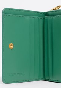 Interno di un portafoglio verde in pelle con più scomparti per carte, cuciture visibili e chiusura a pulsante dorato. Nome del marchio impressa.