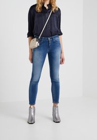 Chemise boutonnée bleu marine avec poches avant, associée à un jean skinny bleu moyen et des bottines argentées. Petit sac bandoulière beige inclus.