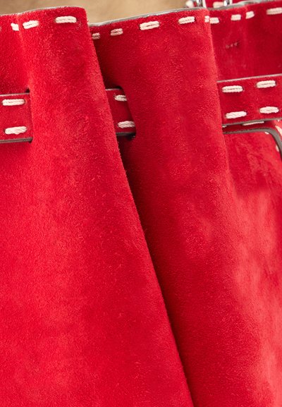 Κοντινό πλάνο κόκκινων μπότες από σουέτ με λευκά νήματα αντίθεσης και λεπτομέρεια με λουράκι γύρω από την περιοχή του αστραγάλου.