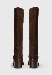 Bottes montantes en daim marron avec un talon carré et des détails de couture verticale ; texture lisse et design à bout arrondi.