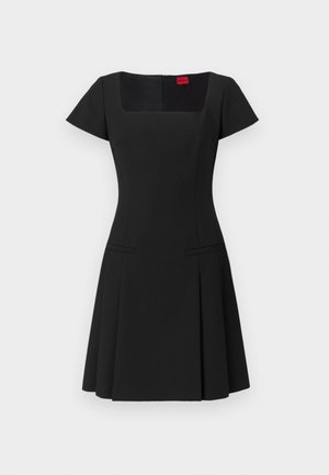 Μαύρο φόρεμα με τετράγωνη λαιμόκοψη, κοντά μανίκια και εφαρμοστό κορσάζ. Έχει φαρδύ φουστάνι και δύο πλευρικές τσέπες. Είναι κατασκευασμένο από μαλακό ύφασμα.