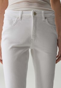 Jeans in denim bianco slim fit, dotati di tasche frontali, dettagli di cucitura discreti e chiusura con bottone in metallo in vita.