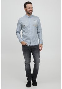 Lyseblå langermet skjorte med knapper, dekorert med grafisk tekst og logo, kombinert med mørkegrå jeans og svarte sko.