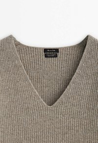 Pull en laine et cachemire beige côtelé avec un col en V et une étiquette noire cousue à l'intérieur du col.