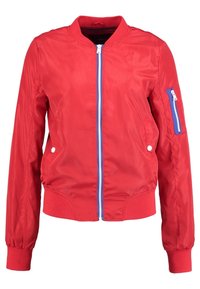 Veste bomber rouge en tissu lisse et brillant; comporte une fermeture éclair bleue, des poignets et un ourlet côtelés, ainsi qu'une poche zippée sur la manche.