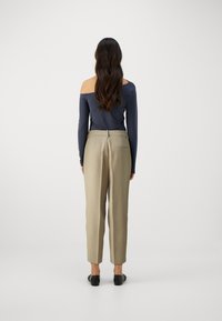 Long-sleeve, off-shoulder navy top paired with high-waisted, tailored beige trousers. Smooth fabric texture, fitted shape, and classic design.