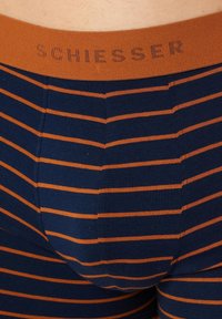 Marineblauwe katoenen boxershorts met dunne oranje strepen en een effen oranje tailleband met de tekst "SCHIESSER" erop gedrukt.