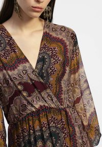Abito a maniche lunghe con scollatura a V, motivo floreale a paisley in tonalità terrene di bordeaux, verde e oro, con vita aderente e tessuto fluido.