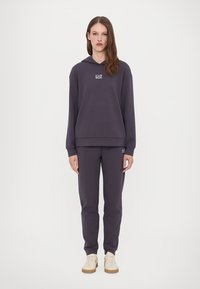Mörkgrå hoodie med "EA7"-logotyp, löst snitt, kombinerad med matchande joggerbyxor. Slät tyg, ribbade mudd och nederkant. Sneakers ingår.