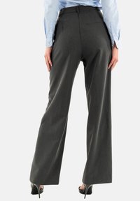 Pantaloni grigi su misura con un design a gamba larga, realizzati in un tessuto liscio; presentano una vita alta e due tasche posteriori. Indossati con tacchi alti.