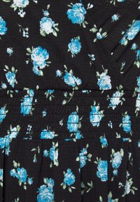Tissu noir avec motif floral bleu et blanc et détail de taille élastique froncée.